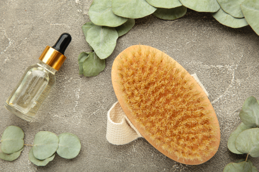 a dry brush with a small bottle of dry brushing oil next to it surrounded by eucalyptus leaves.