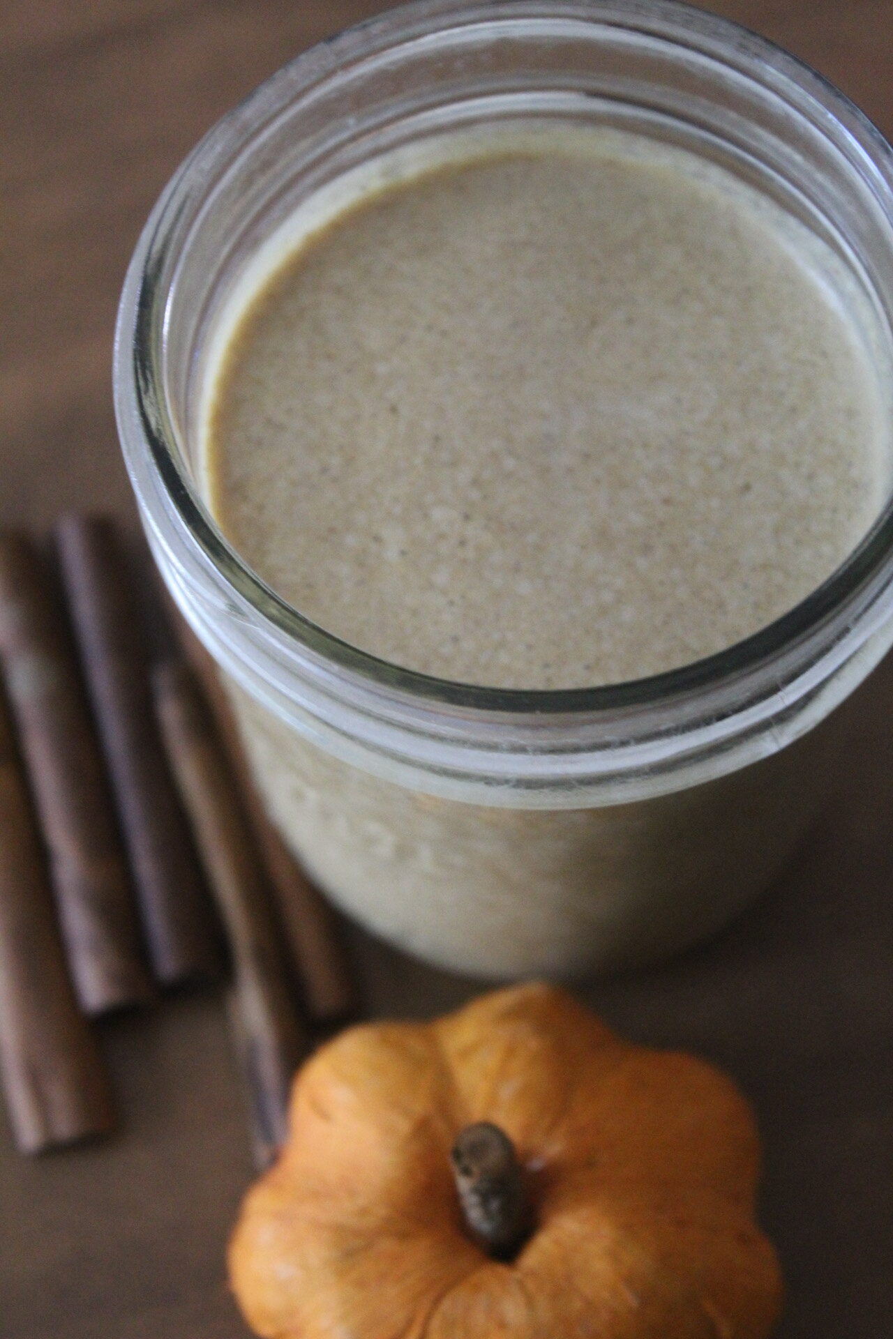 a glass with a pumpkin pie smoothie in it, next to an orange pumpkin and cinnamon sticks.