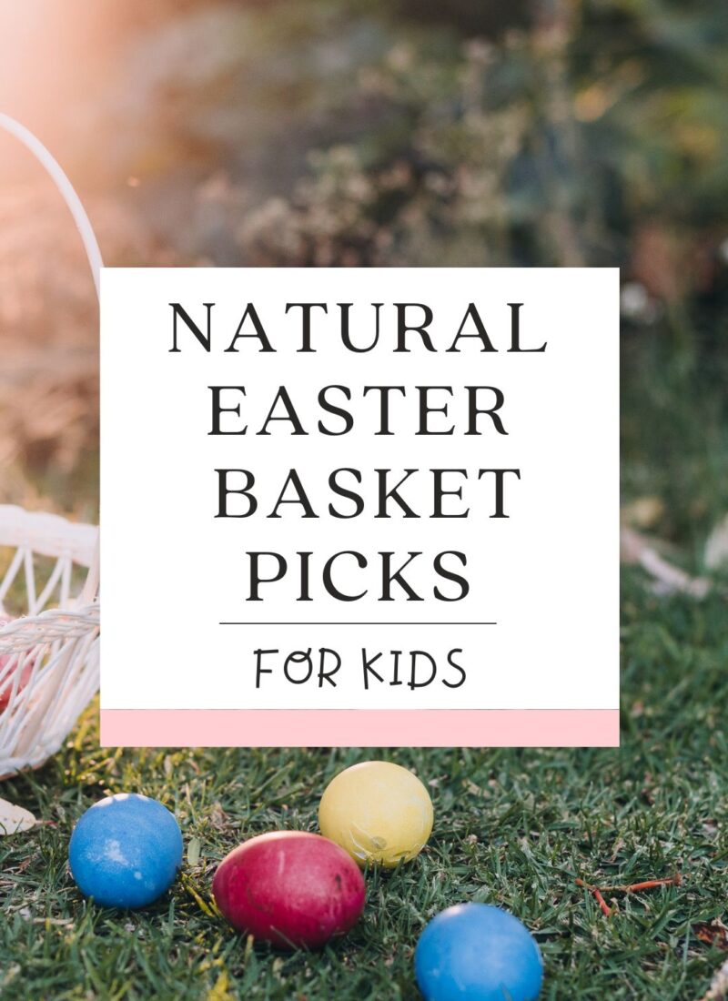 a white Easter Basket sitting on green grass with 4 colored eggs (red, blue and yellow) in front of it on the ground.