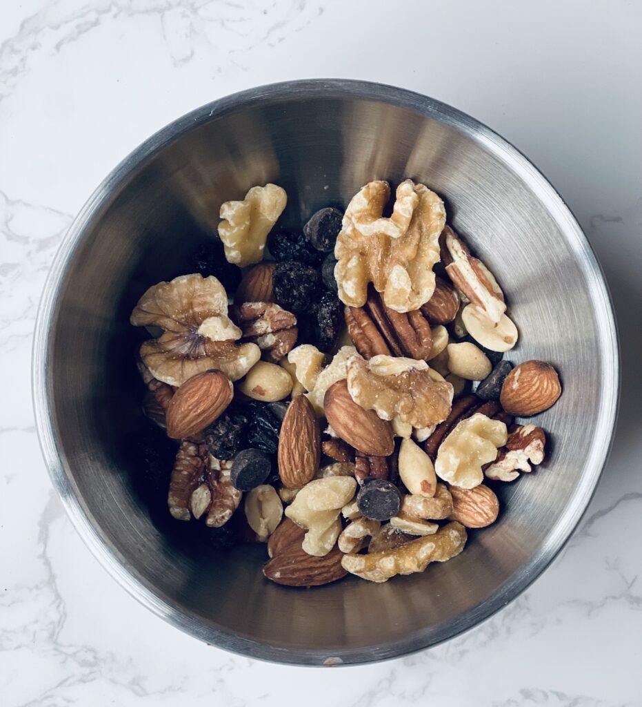 A stainless steel bowl of a homemade nut mix with walnuts, almonds, pecans, peanuts and mini dark chocolate chips.