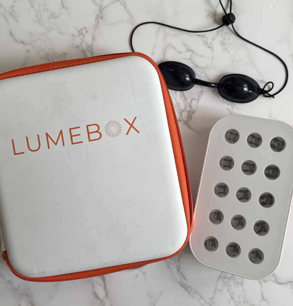 a red light therapy box with it's lumbox carrier container next to it with a pair of black eye goggles above it. 