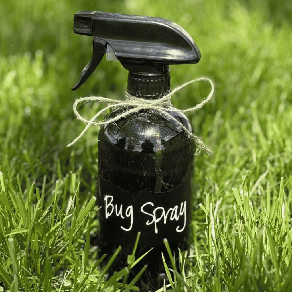 Amber glass bottle of DIY bug spray sitting in a field of long green blades of grass