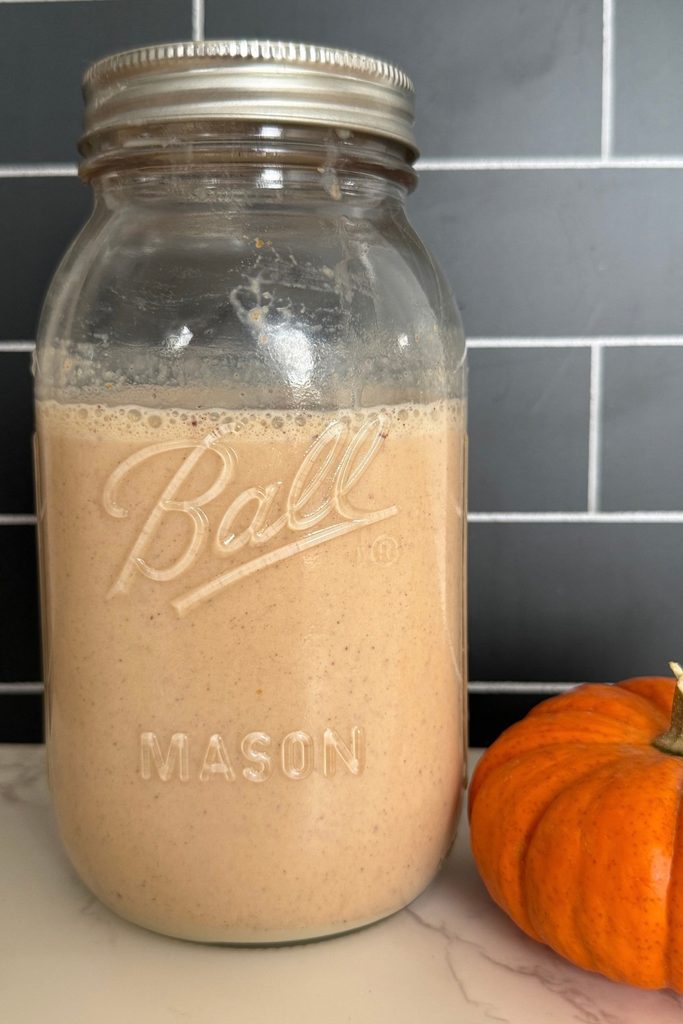 A ball mason jar full of homemade pumpkin spice creamer wiht an orange mini pumpkin on the right side of it.